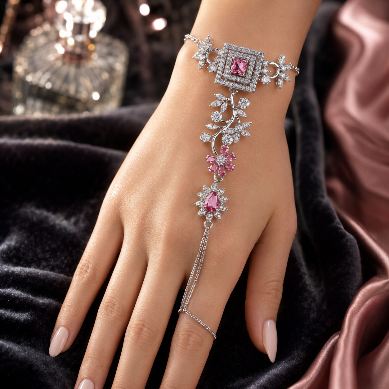 A close-up of a hand wearing an ornate silver-toned chain bracelet with pink gemstones and clear stones, styled against dark velvet fabric and satin.