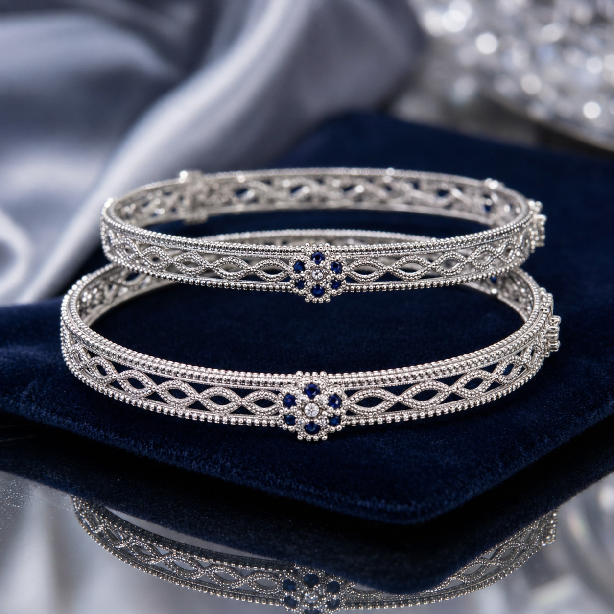 Two silver filigree bangles with blue stone floral accents, displayed on a dark blue velvet cushion.