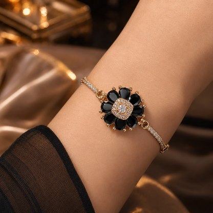 A close-up of a gold-plated bracelet with a flower motif featuring black stones and a clear center stone, worn on a person's wrist.