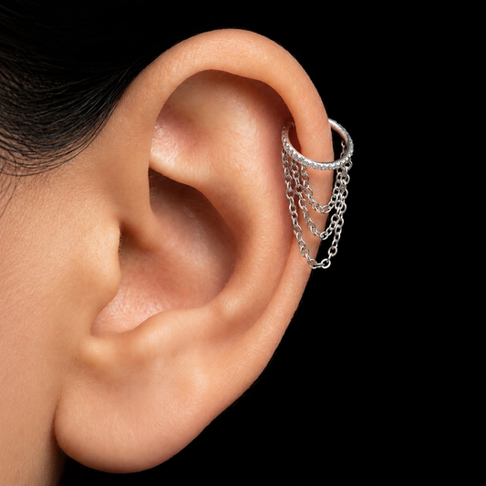 A close-up of a person's ear wearing a silver cartilage hoop earring with three dangling chain strands, set against a solid black background.