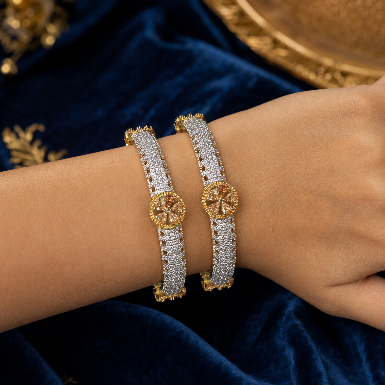 Two gold and silver bangle bracelets with pavé-set stones, worn on a person's wrist against a dark blue velvet background.