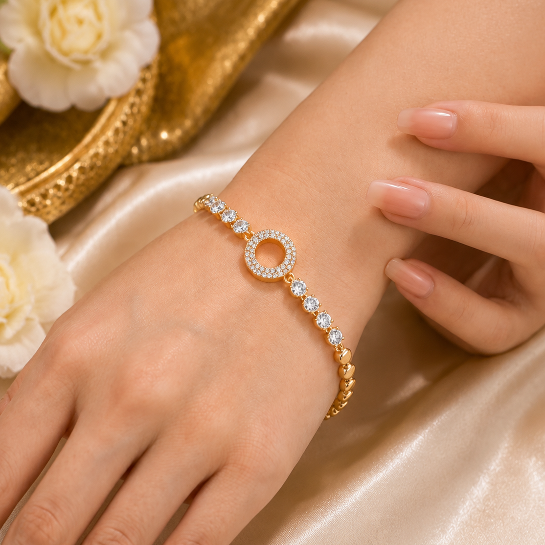A gold bracelet with a central diamond-pierced circle and small clear stones along the band, shown worn on a woman's wrist against a satin fabric background with decorative flowers.