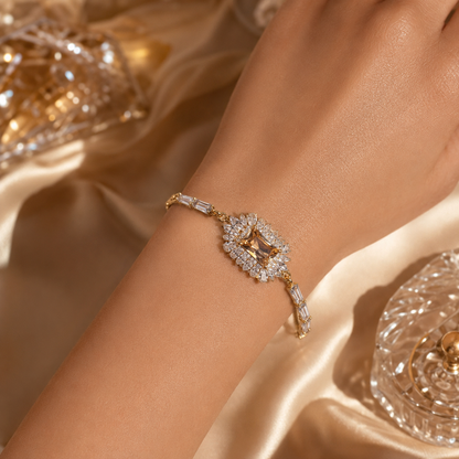 A gold-toned bracelet with a central star-shaped crystal cluster surrounded by small clear stones, shown worn on a person's wrist against a warm champagne satin background.