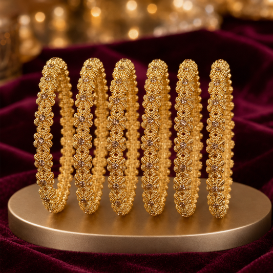 Six ornate gold bangles with intricate floral detailing and small clear stones, arranged upright on a round gold display stand against a deep burgundy velvet background with blurred golden bokeh.