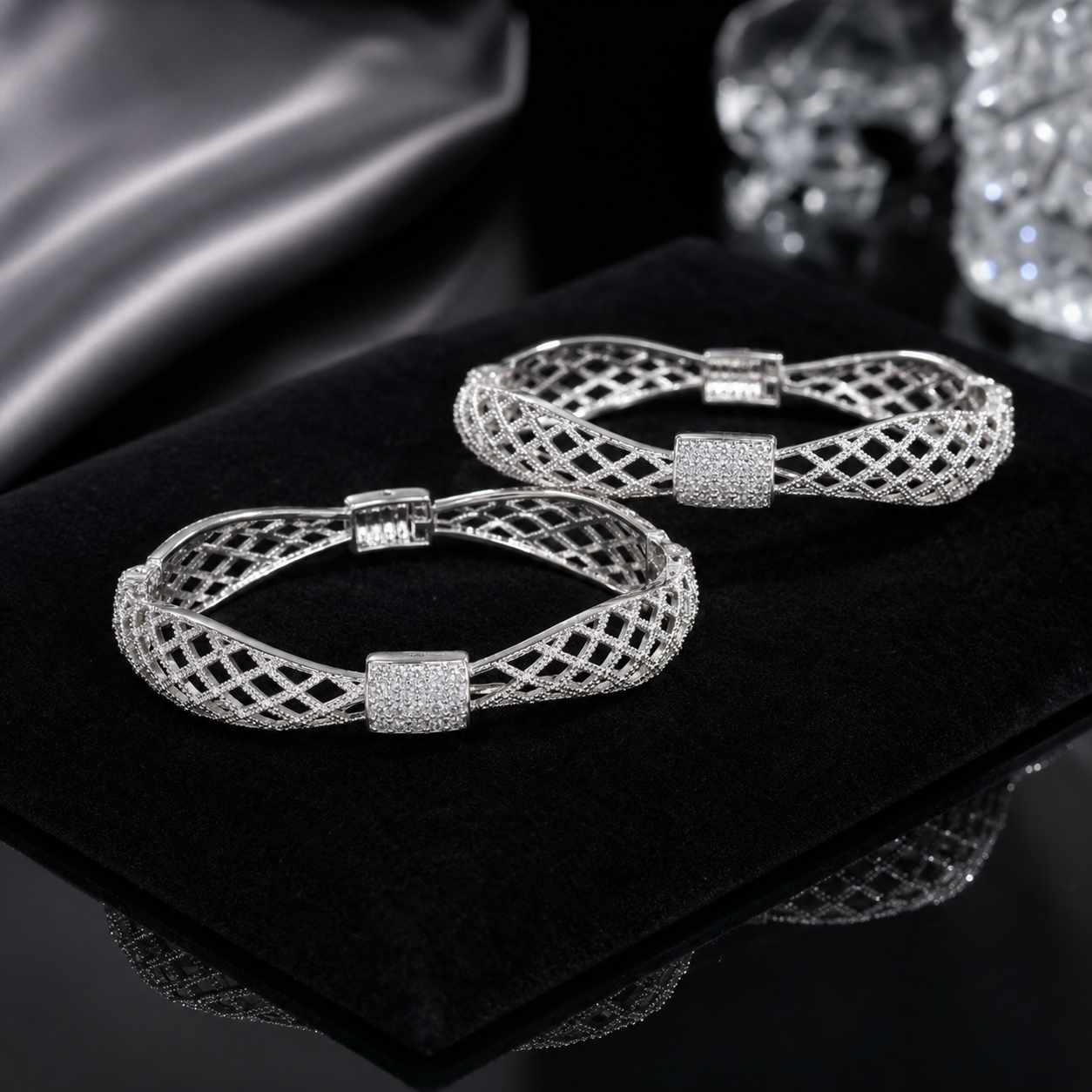 A pair of silver-toned filigree bangle bracelets with square crystal-encrusted centers, displayed on a black velvet jewelry box.