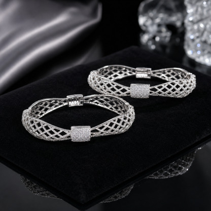 A pair of silver-toned filigree bangle bracelets with square crystal-encrusted centers, displayed on a black velvet jewelry box.