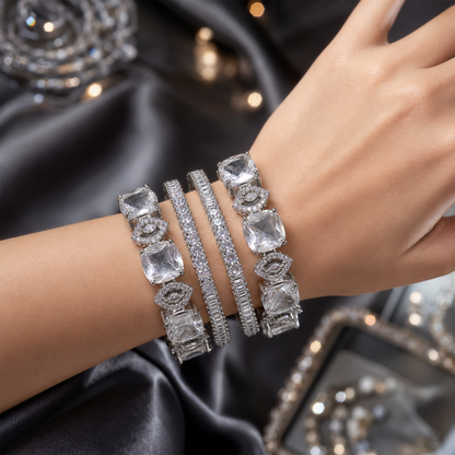 A close-up of a person's wrist wearing four silver-toned bracelets with clear gemstones, set against a dark satin fabric background.