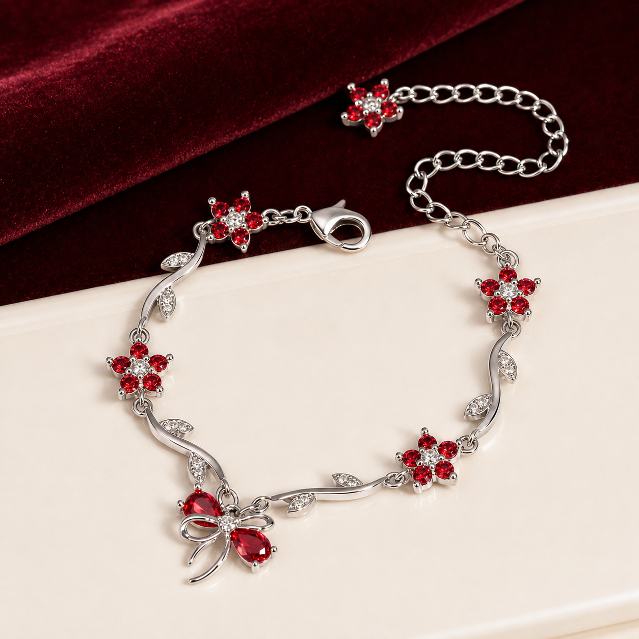 A silver-toned vine bracelet decorated with red crystal flowers and a bow-shaped centerpiece, displayed on a cream surface with a dark red velvet cloth in the background.